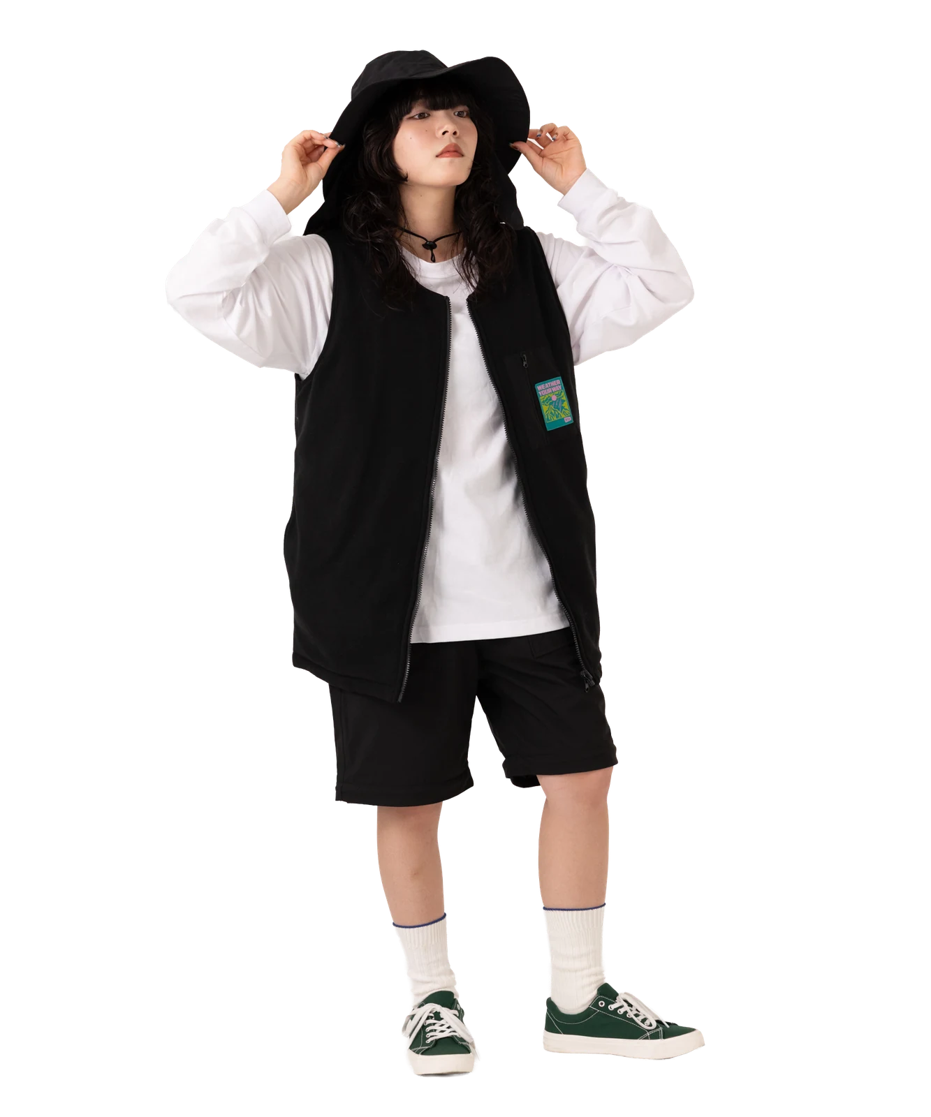 帽子に手を添えたベストとショートパンツの全身コーデ